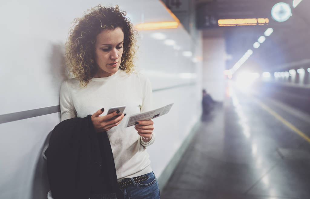 Viajante mulher mensagens de texto de um smartphone enquanto está esperando com uma mala em um aeroporto ou uma estação ferroviária
 - Foto, Imagem