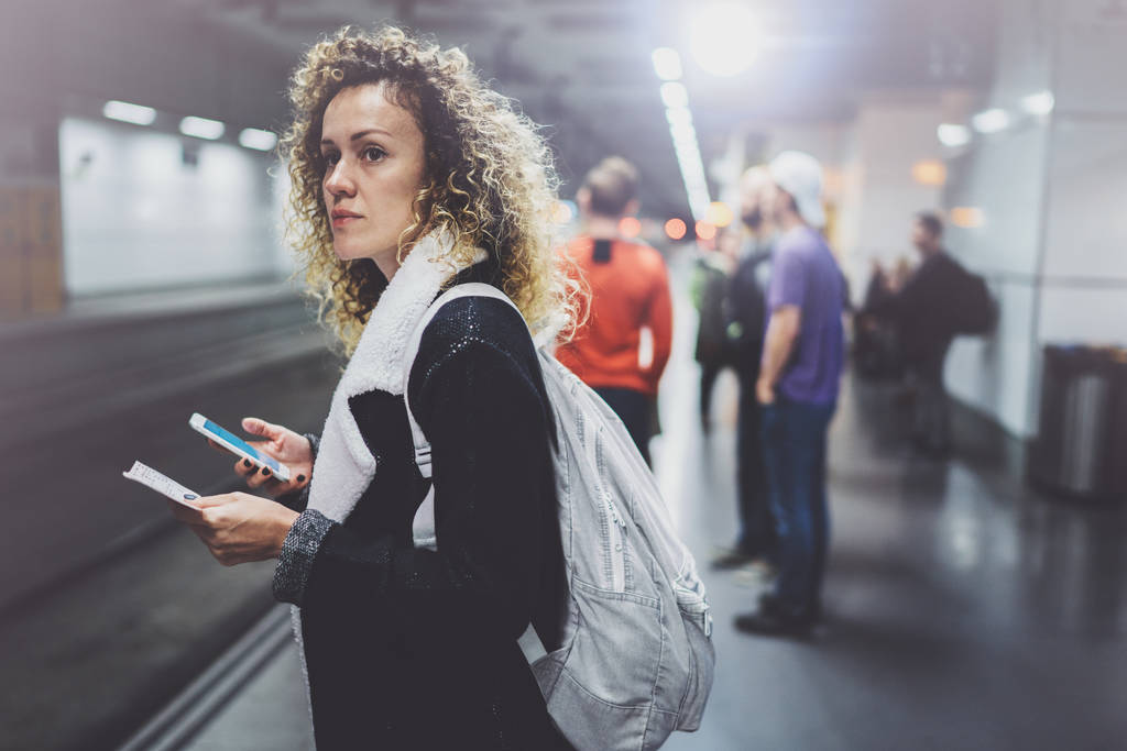 Привлекательная женщина с рюкзаком на транзитной платформе с помощью смартфона для фото железнодорожного билета во время ожидания поезда на станции метро
. - Фото, изображение