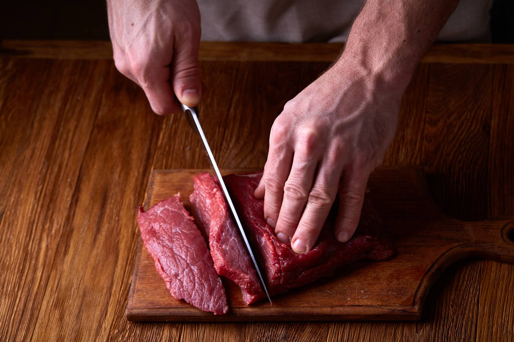 Сильний професійний чоловік рук різання сирого яловичого стейка, вибірковий фокус, крупним планом
 - Фото, зображення