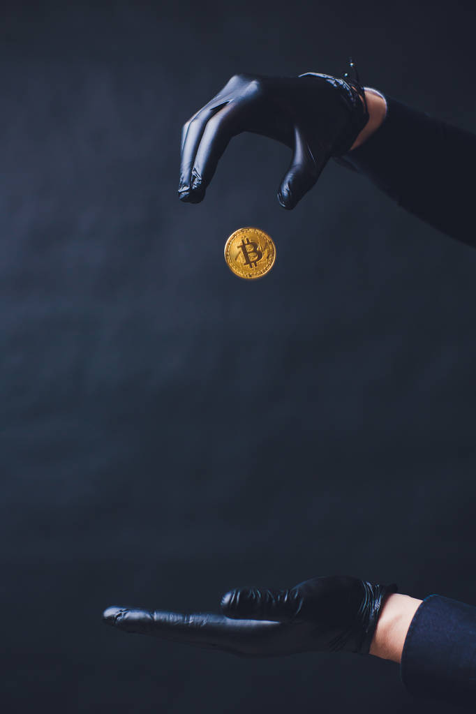 Bitcoin. Рука крапель золоті монети. Руки в чорні рукавички. Концепція падіння крипто валюти. Ізольовані на чорному фоні. - Фото, зображення