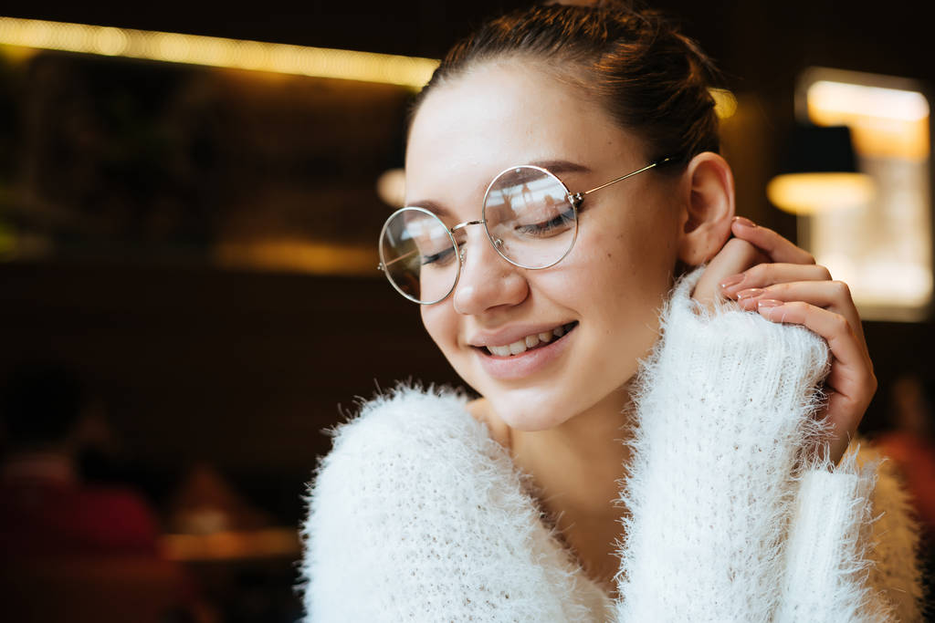 放課後カフェで座っている白いセーターを着て、メガネで美しい少女学生笑顔 - 写真・画像