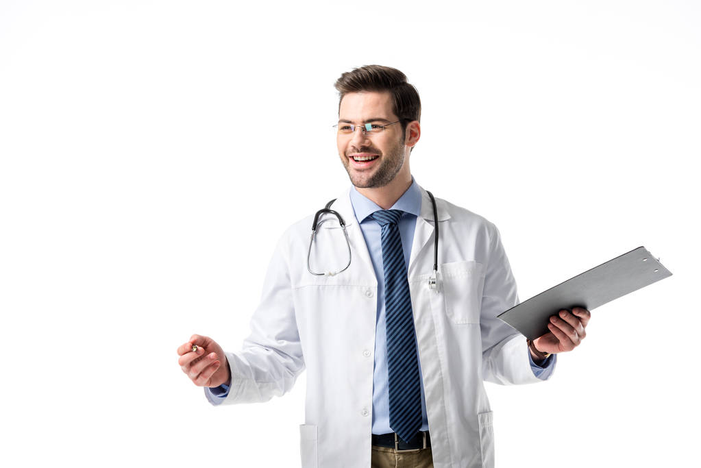 Cheerful doctor wearing white coat with stethoscope and holding clipboard isolated on white - Photo, Image