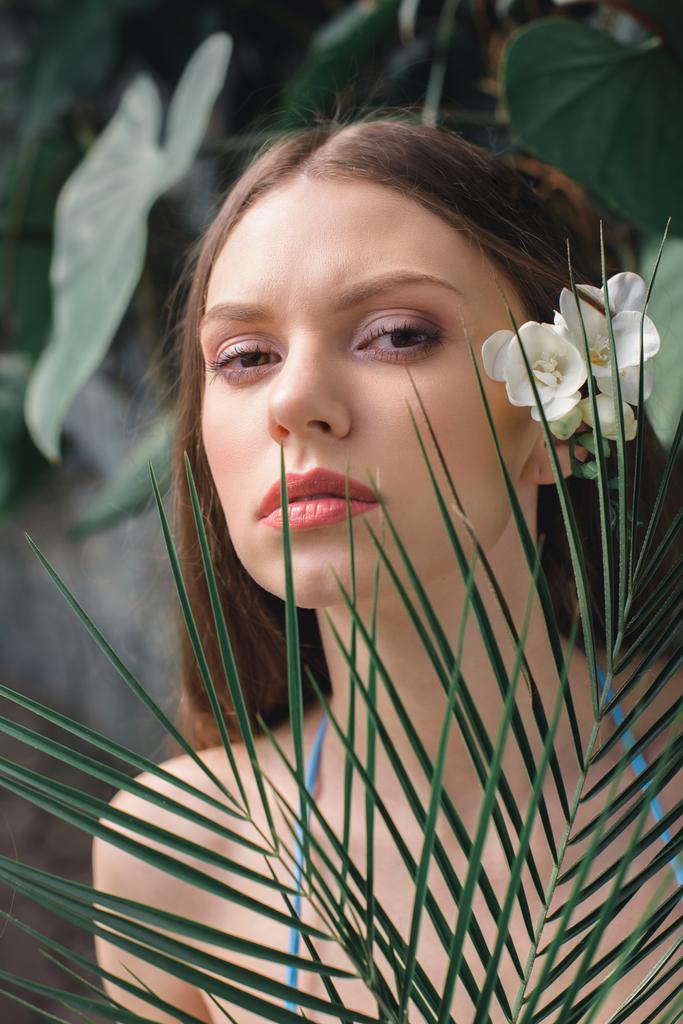 attrayant jeune femme avec fleur dans les cheveux posant avec des feuilles de palmier sur station tropicale
 - Photo, image