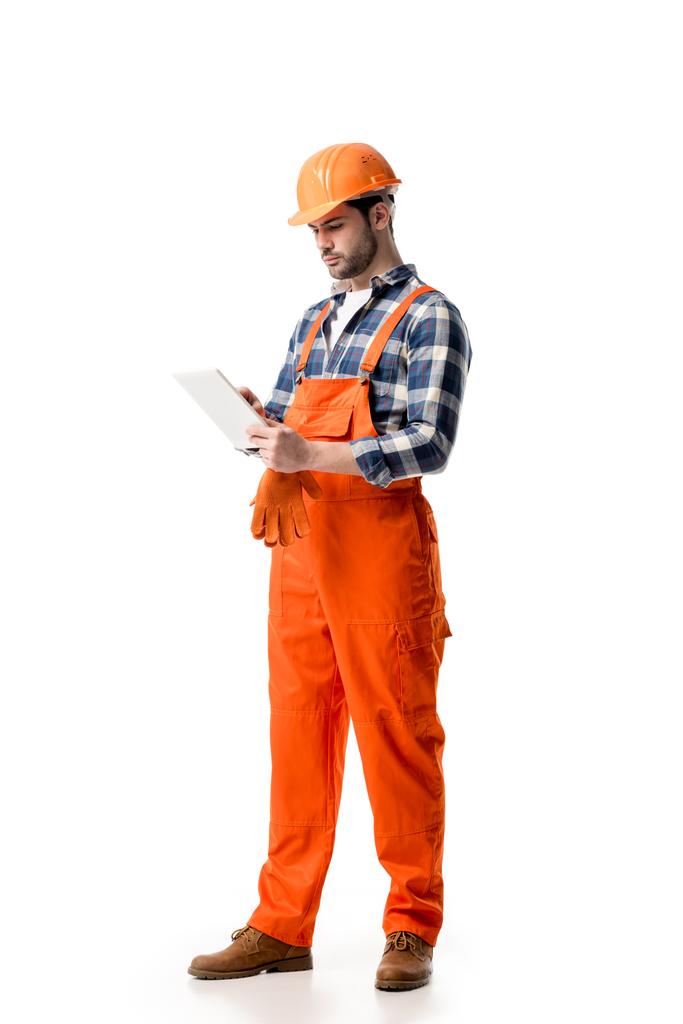 Jonge reparateur in een oranje overall en harde hoed met behulp van digitale tablet geïsoleerd op wit - Foto, afbeelding