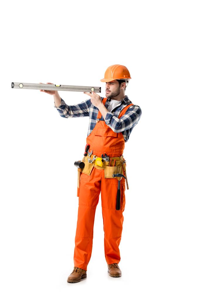 рабочий в оранжевый общий и каска проверки уровень духа изолированы на белом
 - Фото, изображение