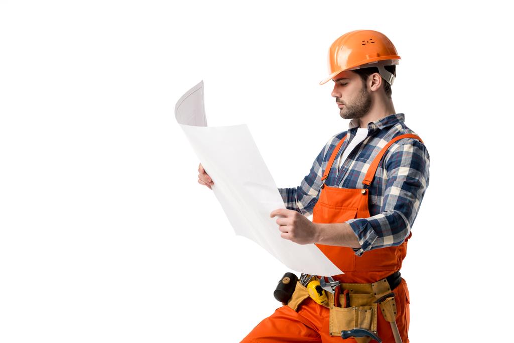Reparateur in orangefarbenem Overall und Helm schaut auf Blaupause isoliert auf weißem Grund - Foto, Bild