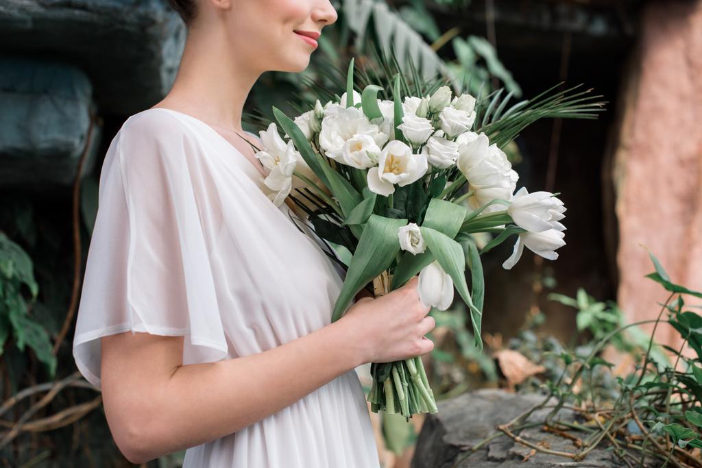 περικοπεί προβολή της νύφης, θέτοντας σε λευκό φόρεμα με γαμήλια ανθοδέσμη - Φωτογραφία, εικόνα