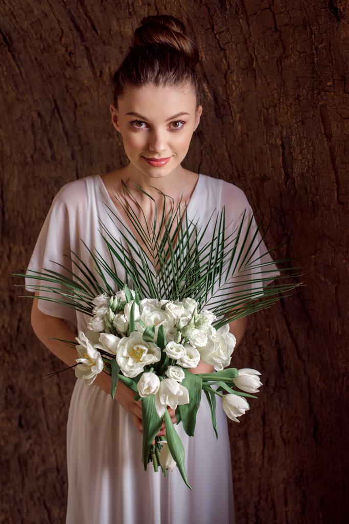 白いドレスの結婚式のブーケとポーズで魅力的な若い女性 - 写真・画像