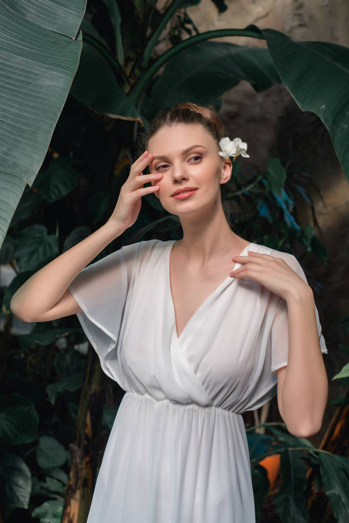 attrayant tendre femme en robe blanche avec fleur dans les cheveux posant dans le jardin tropical
 - Photo, image