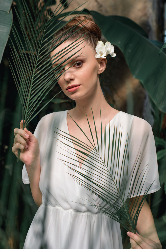 belle fille en robe d'été blanche posant avec des feuilles de palmier tropical
 - Photo, image