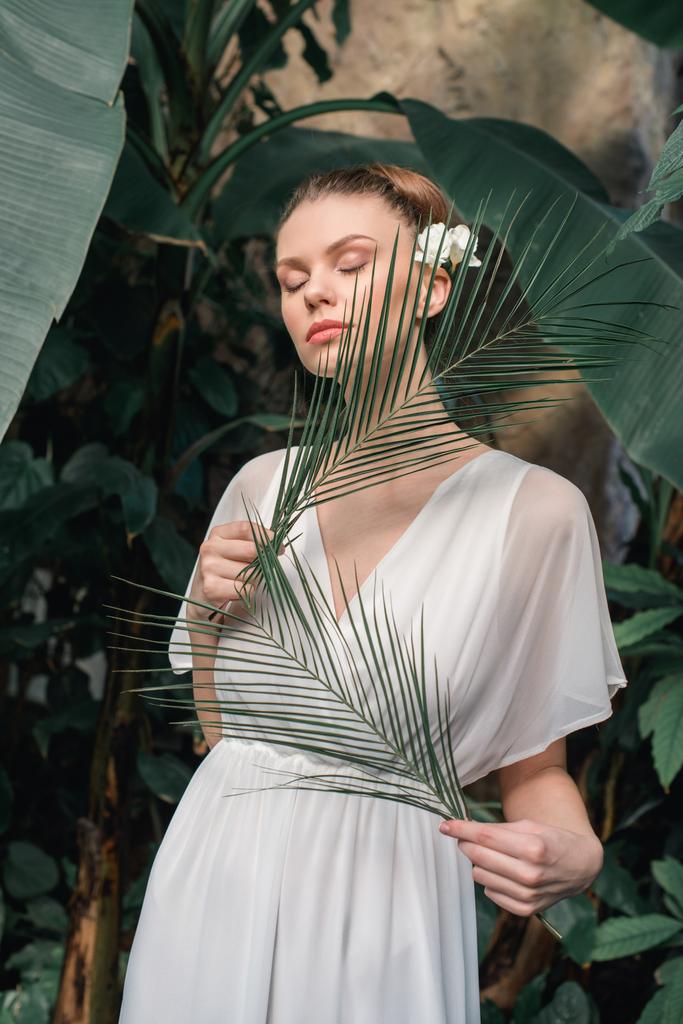 нежная девушка в белом летнем платье позирует с тропическими пальмовыми листьями
 - Фото, изображение
