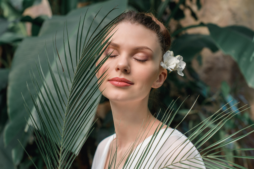 piękna dziewczyna z zamkniętymi oczami pozowanie w biały Letnia sukienka z liści palmowych tropikalny - Zdjęcie, obraz