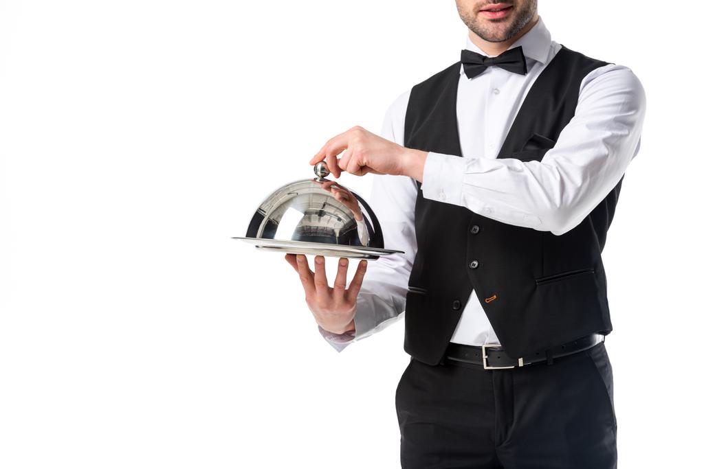 Μερική άποψη του σερβιτόρου στο κοστούμι γιλέκο κρατώντας δίσκο σερβιρίσματος στα χέρια που απομονώνονται σε λευκό - Φωτογραφία, εικόνα