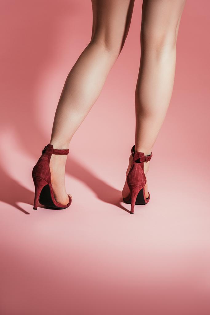 vista trasera de las piernas de la mujer en sandalias de tacón alto con estilo sobre fondo rosa
 - Foto, Imagen
