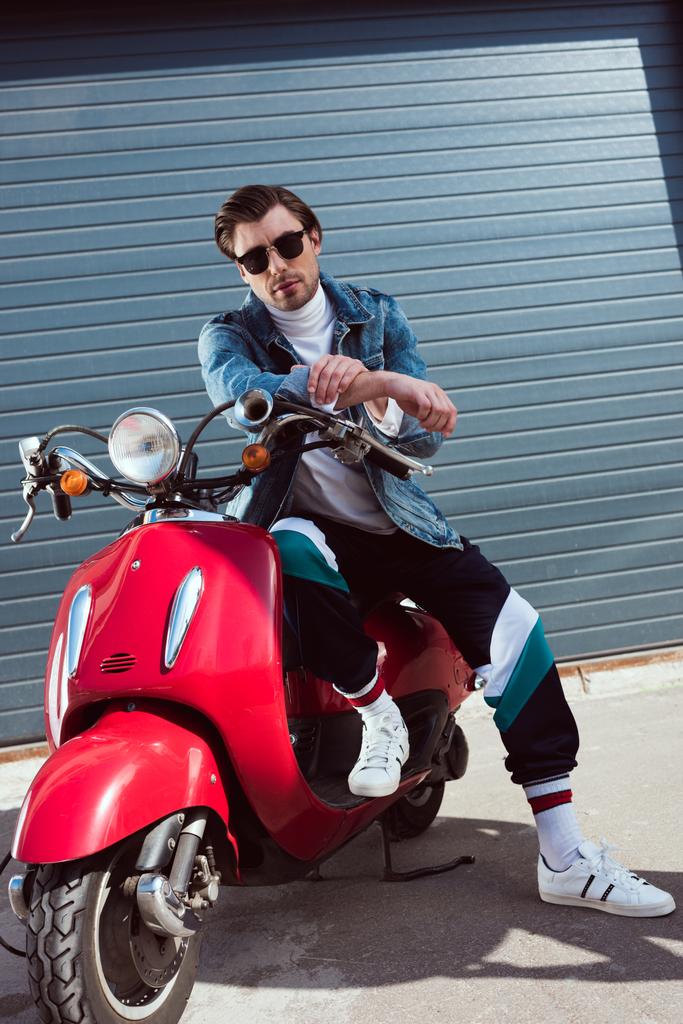 jovem bonito em jaqueta de ganga e calças de pista sentado em scooter vermelho vintage
 - Foto, Imagem