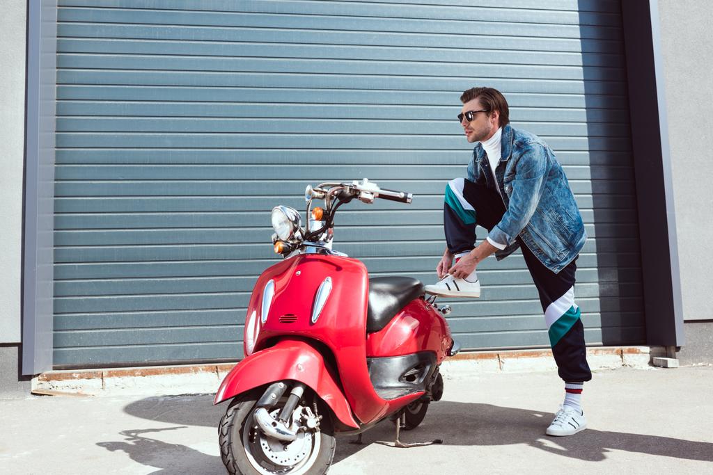 bello giovane in abiti vintage con scooter rosso sdraiato su lacci
 - Foto, immagini