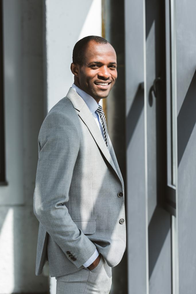 portrait de beau jeune homme d'affaires afro-américain debout avec la main dans la poche et souriant à la caméra
 - Photo, image
