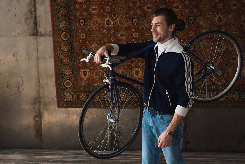 yol bisikleti omuz önünde duvara asılı halı üzerinde taşıyan vintage giyim mutlu genç adam - Fotoğraf, Görsel