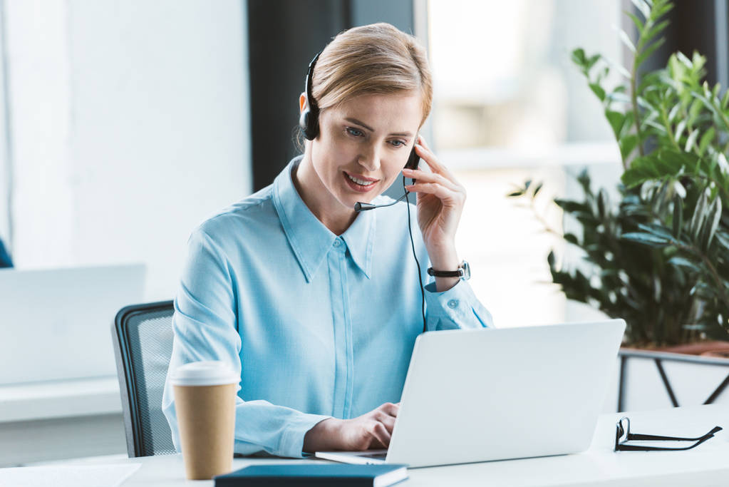 Glimlachende zakenvrouw in hoofdtelefoon laptop gebruiken in office  - Foto, afbeelding