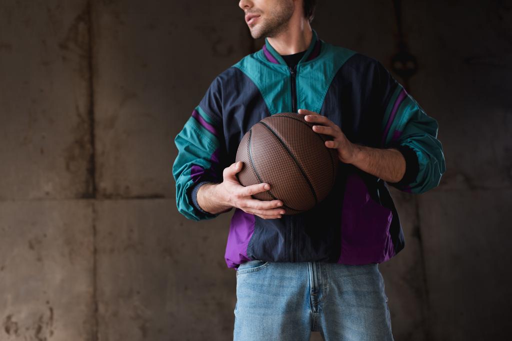 обрезанный снимок молодого человека в винтажном ветрянике с баскетбольным мячом
 - Фото, изображение