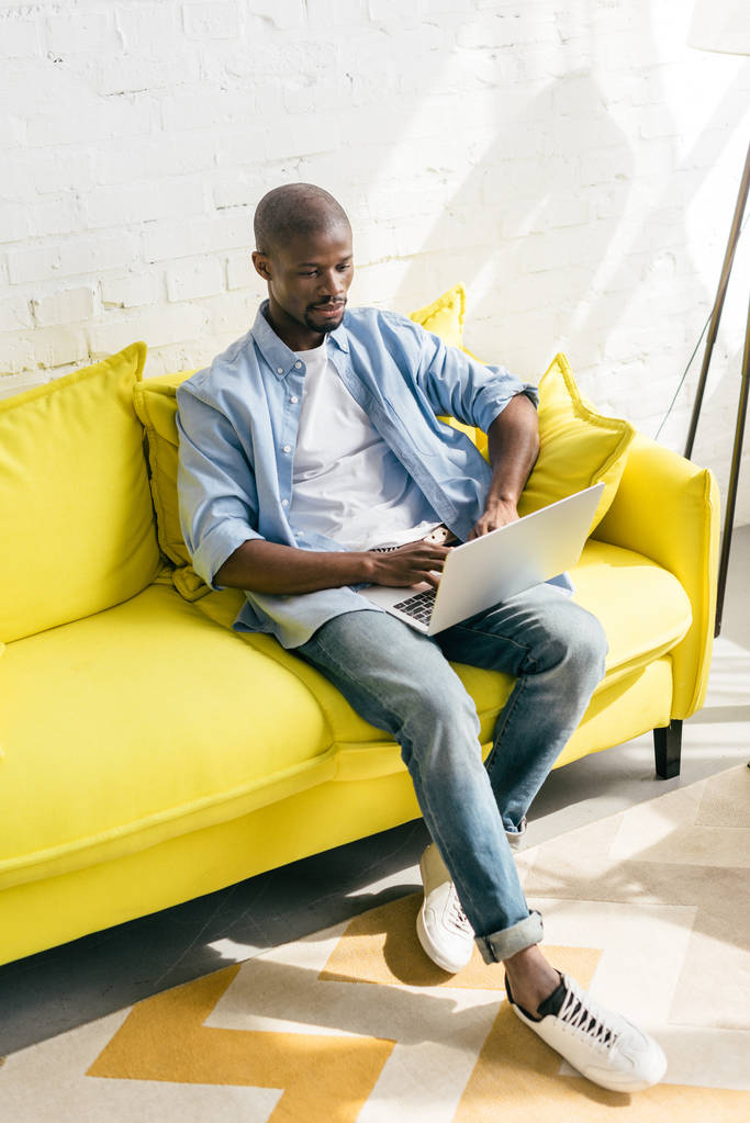 uomo afro-americano che utilizza il computer portatile sul divano di casa
 - Foto, immagini