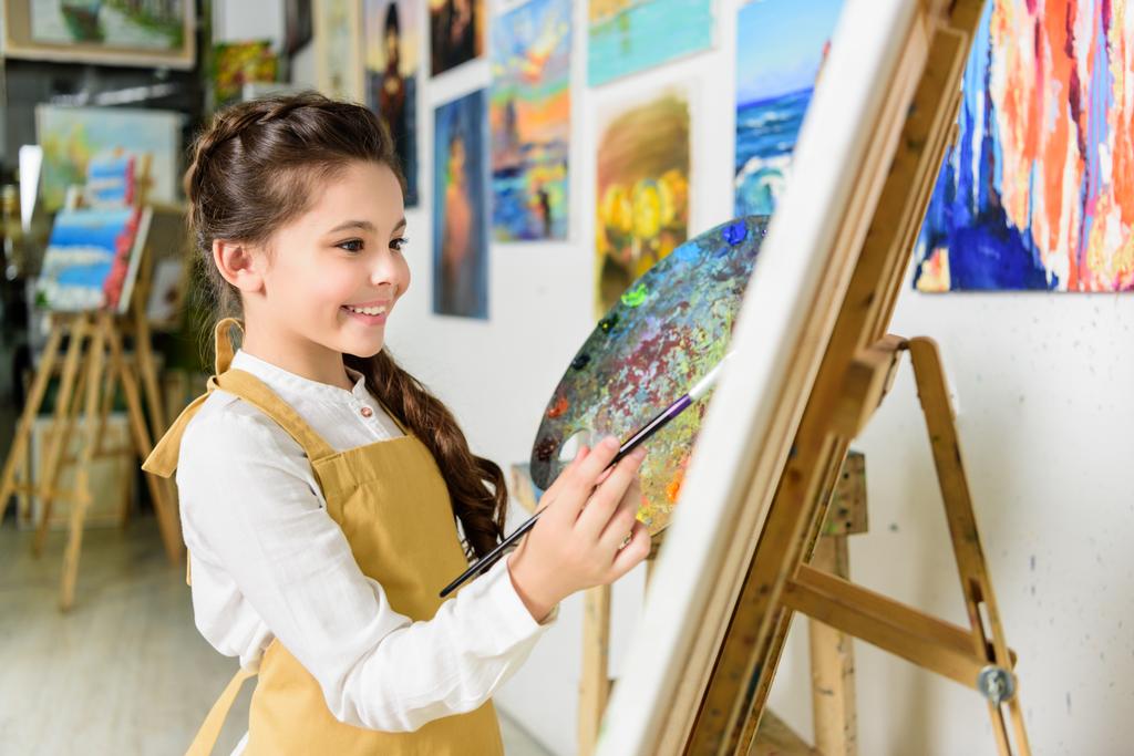 side view of smiling kid painting in workshop of art school - Photo, Image
