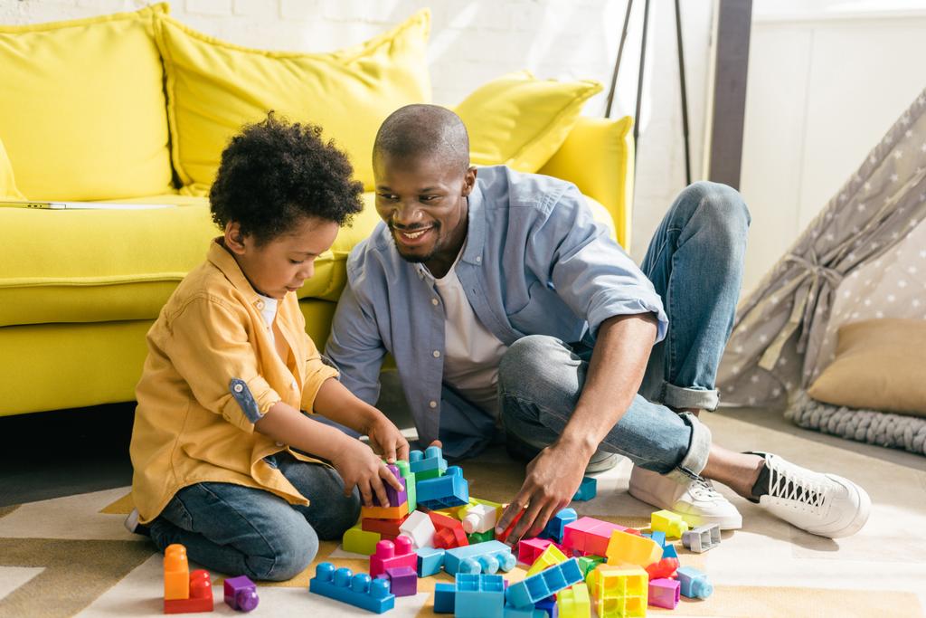 s úsměvem africké americkému otci a malý syn s barevnými bloky spolu hrají doma - Fotografie, Obrázek