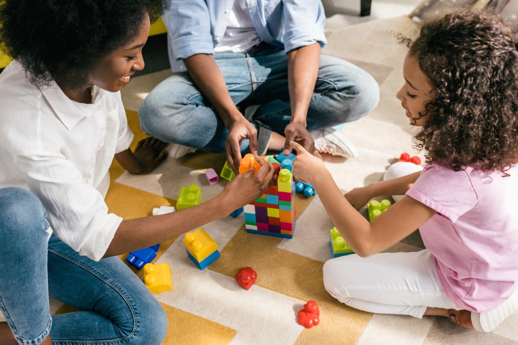 vista parcial de la familia afroamericana jugando con bloques de colores juntos en el piso en casa
 - Foto, imagen
