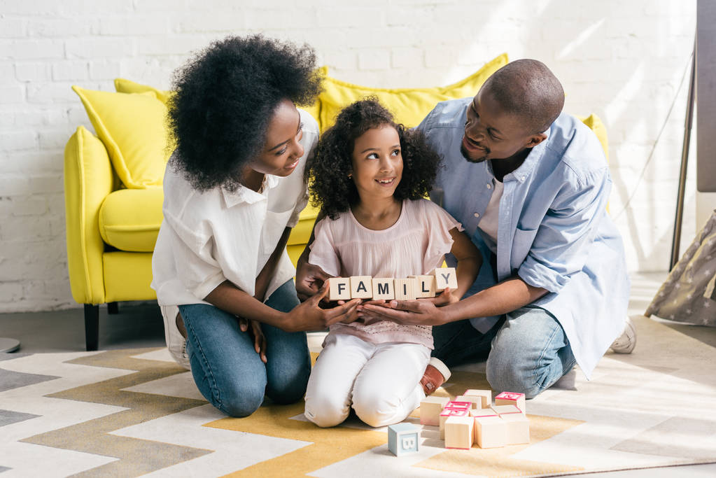 genitori afroamericani e figlia in possesso di blocchi di legno con scritte di famiglia insieme sul pavimento a casa
 - Foto, immagini