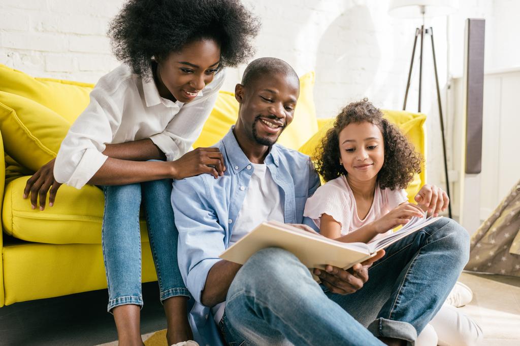 gelukkige Afro-Amerikaanse ouders en dochtertje lezen boek samen thuis - Foto, afbeelding