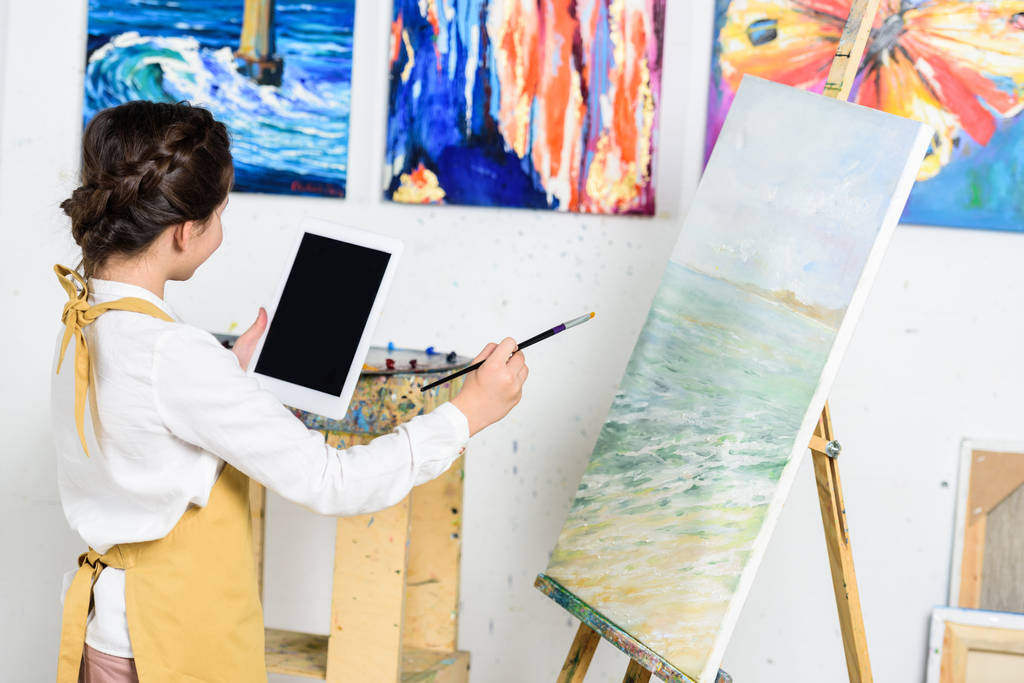 vista lateral del niño mirando tableta y pintura sobre lienzo en el taller de la escuela de arte
 - Foto, Imagen