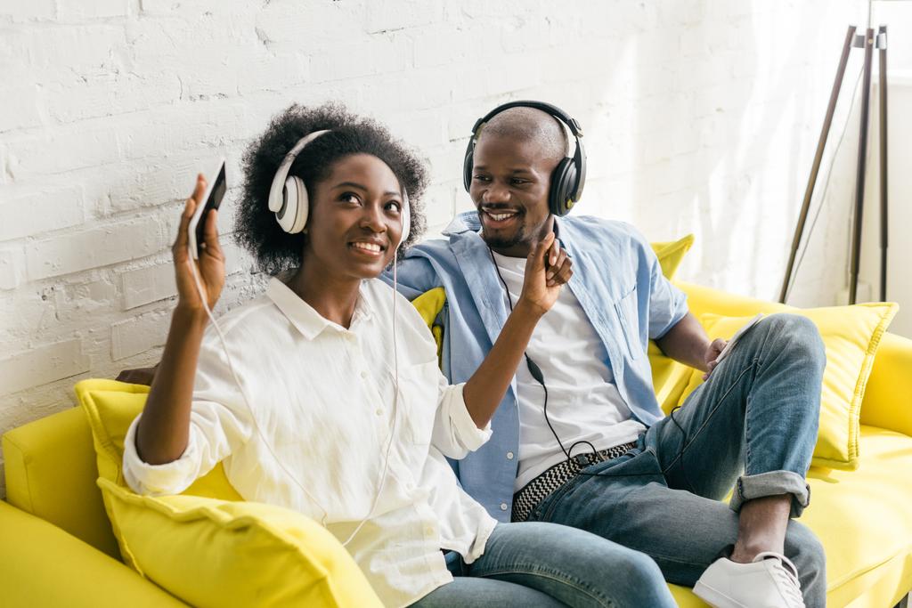 Αφρικανική αμερικανική ακούγοντας μουσική στα ακουστικά ενώ ξεκουραζόταν στον καναπέ στο σπίτι - Φωτογραφία, εικόνα