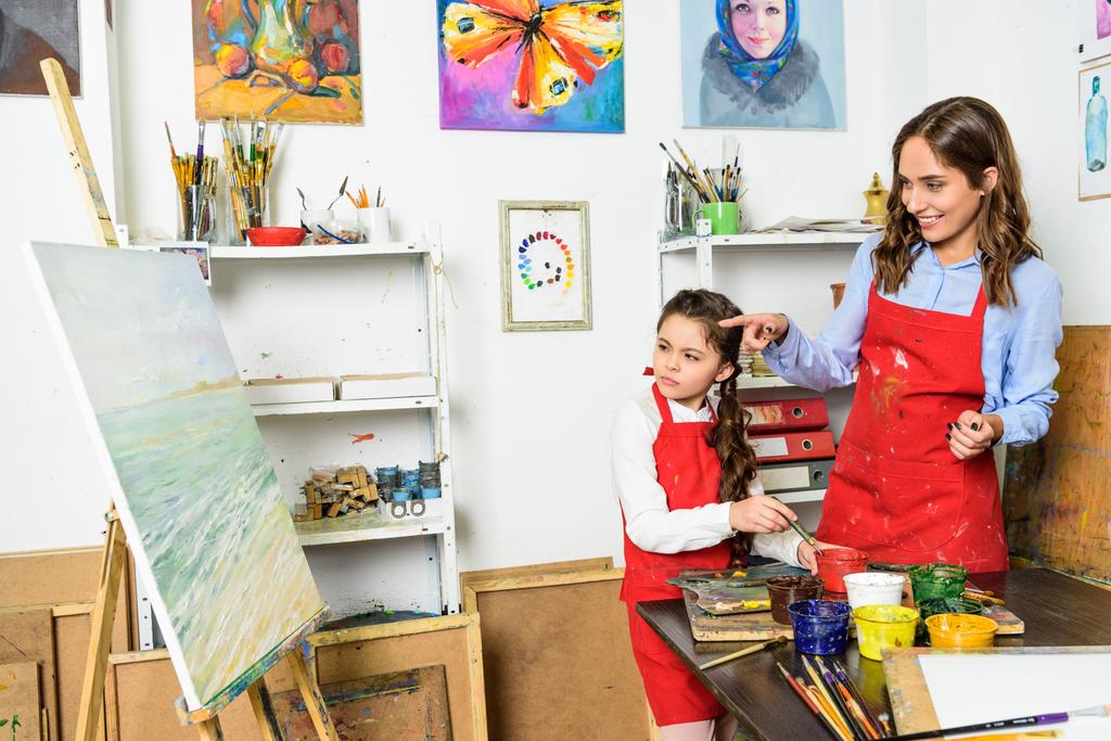 Lehrerin zeigt in Werkstatt der Kunstschule auf Schüler-Leinwand - Foto, Bild