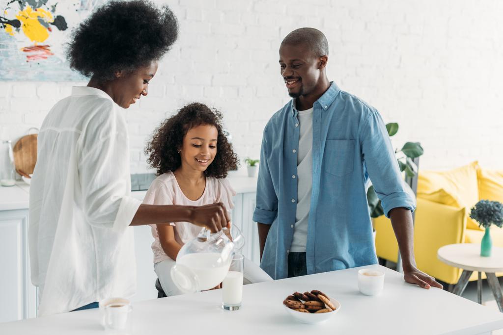 アフリカ系アメリカ人の女性が自宅の台所での近くに家族とグラスにミルクを注ぐ - 写真・画像