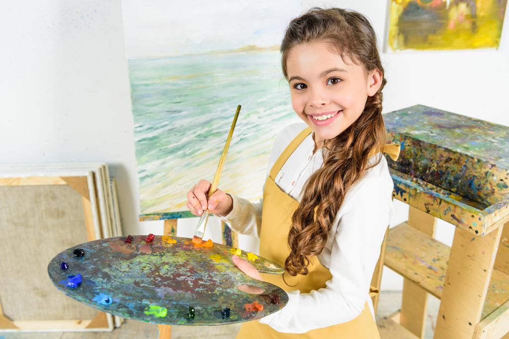 το παιδί κρατώντας πινέλο ζωγραφικής και παλέτα στο εργαστήριο της Σχολής τέχνης - Φωτογραφία, εικόνα