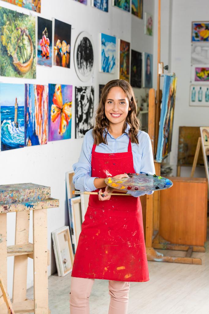 hermosa artista femenina sosteniendo pincel de pintura y paleta en taller
 - Foto, Imagen