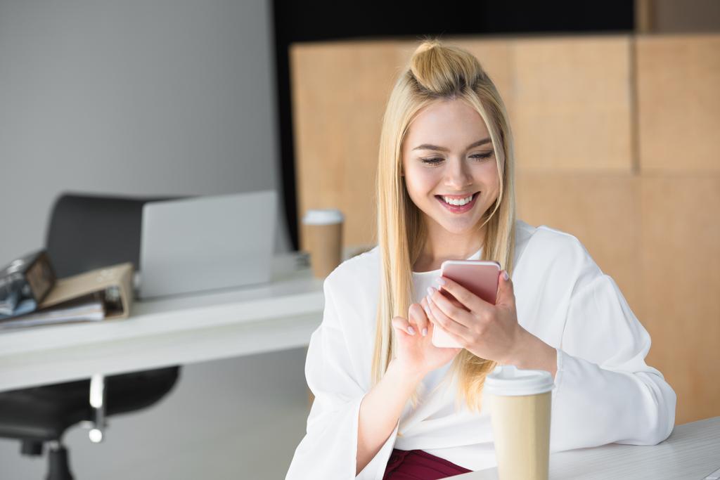 bella sorridente giovane donna utilizzando smartphone sul posto di lavoro
 - Foto, immagini