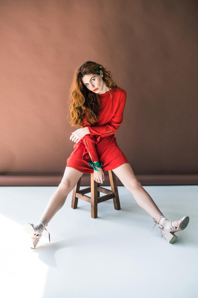 Hosszú vörös haja pózol a fa széklet piros ruhás nő - Fotó, kép