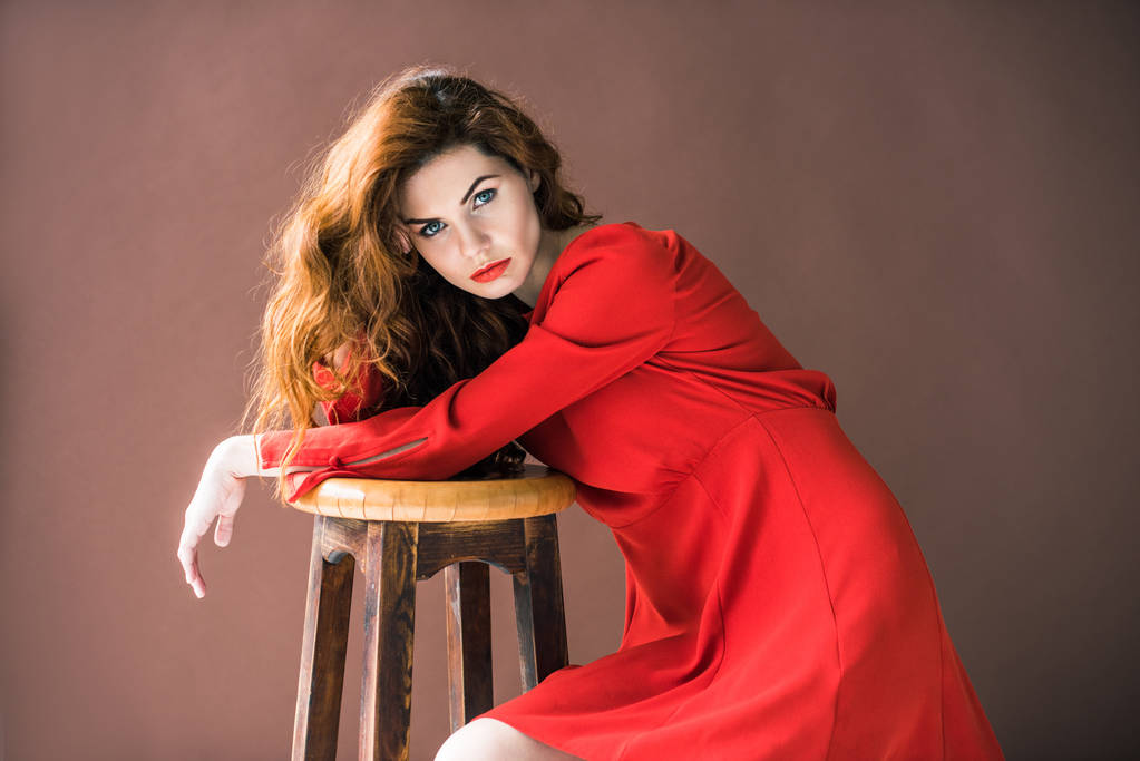 attraktive rothaarige Frau posiert von Holzhocker isoliert auf braunem Hintergrund - Foto, Bild