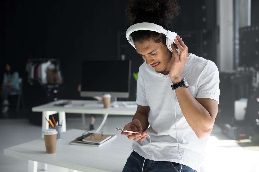 jeune homme afro-américain dans les écouteurs en utilisant smartphone dans le bureau
    - Photo, image