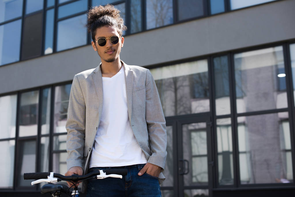 guapo joven afroamericano hombre en gafas de sol de pie con bicicleta en la calle
 - Foto, imagen