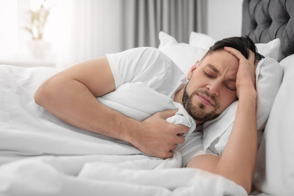 Homem que sofre de dor de cabeça enquanto deitado na cama em casa
 - Foto, Imagem