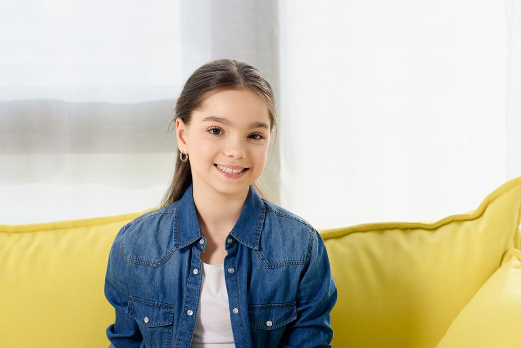 портрет улыбающегося ребенка-подростка, смотрящего в камеру на диване дома
 - Фото, изображение
