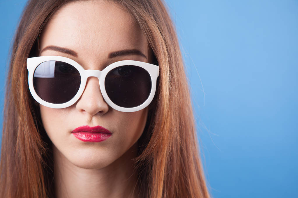 Szép fiatal lány viselni napszemüveget, kék háttérrel - Fotó, kép