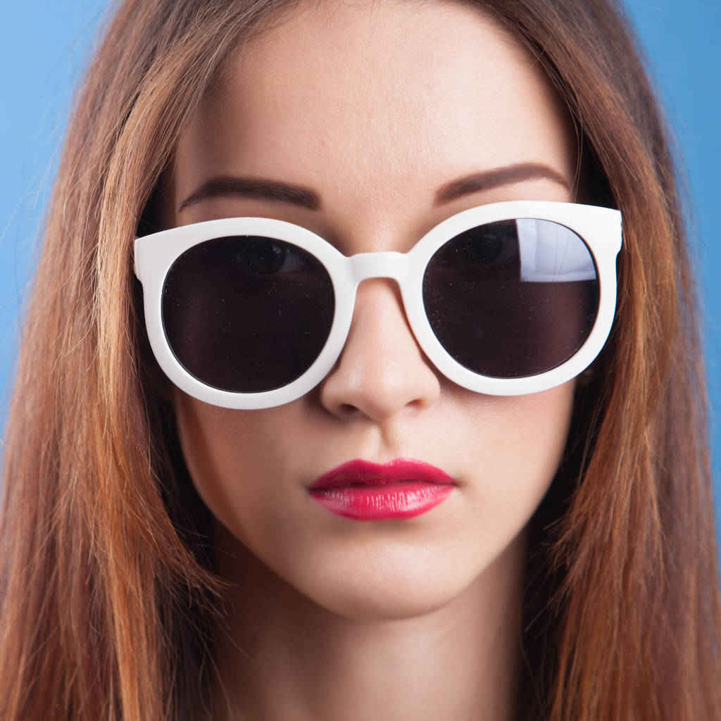 Mooi jong meisje dragen zonnebril op een blauwe achtergrond - Foto, afbeelding