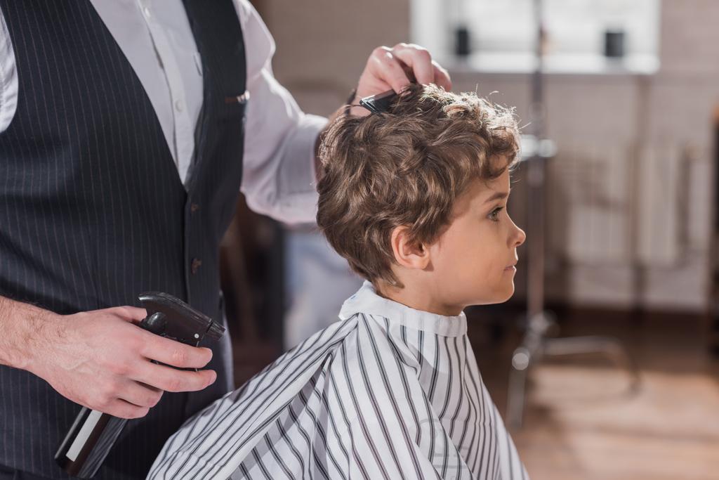 子供理髪店で幼い子供の髪をとかす床屋のショットをトリミング - 写真・画像