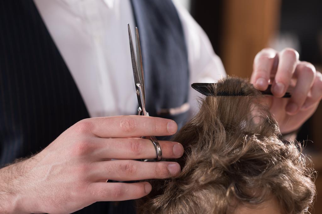 обрезанный снимок парикмахера стригущего волосы маленького ребенка
 - Фото, изображение