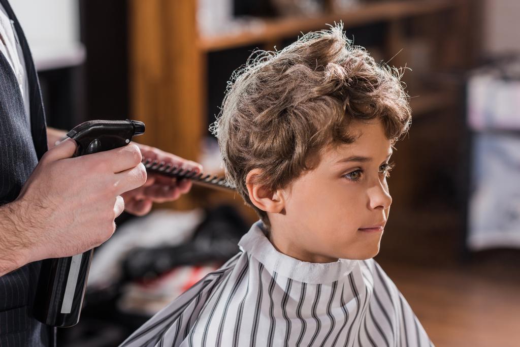 子供理髪店で愛らしい幼い子供の髪をスプレー床屋のショットをトリミング - 写真・画像