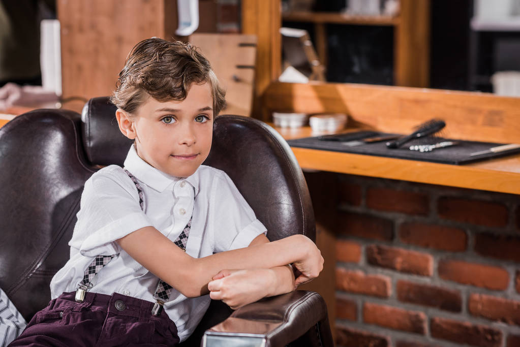 uśmiechający się dzieciak siedzi w fotelu Fryzjer na fryzjera i patrząc na kamery - Zdjęcie, obraz