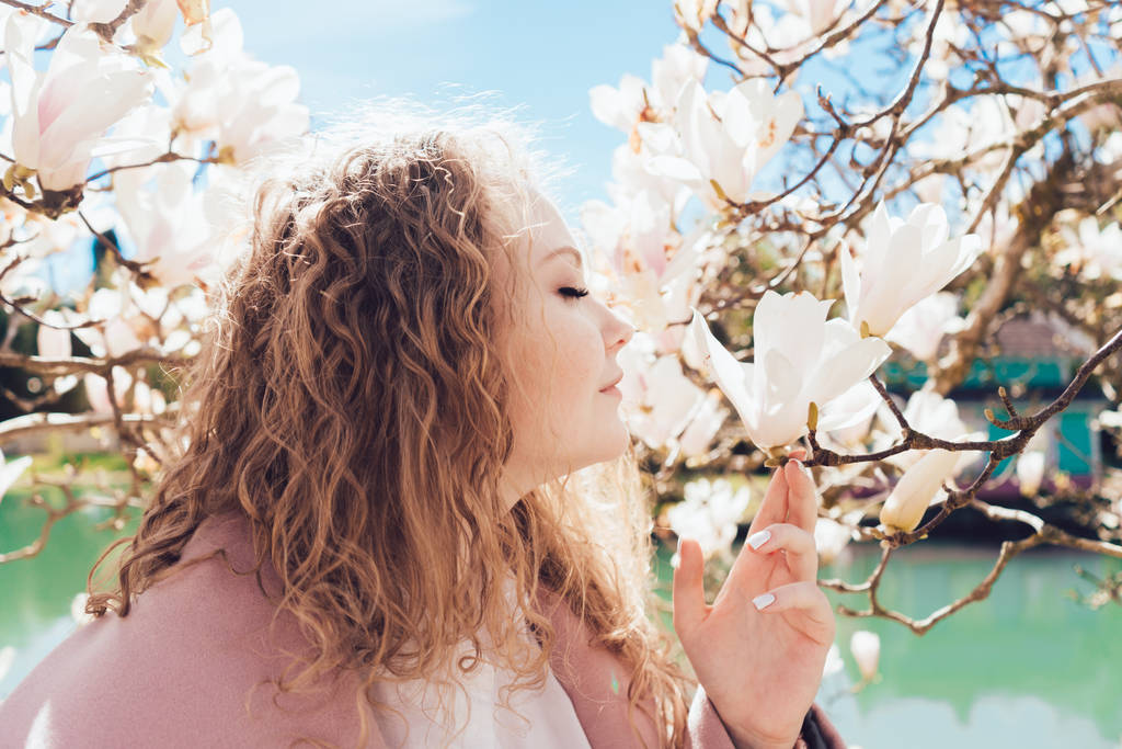 中の若い女性の香り手引き開花マグノリアが公園で彼女の目を閉じ - 写真・画像